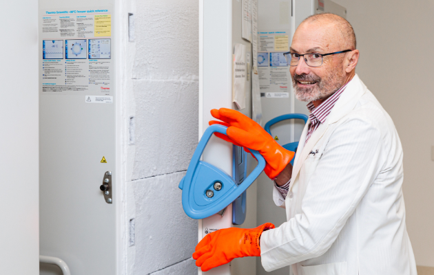 Image shows Professor David Mackey in the research lab wearing bright orange safety gloves and opening a freezer.